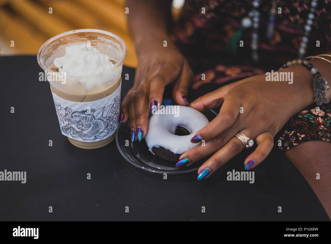 Primo piano della donna nera con le mani il caffè e ciambelle e bella manicure Foto Stock