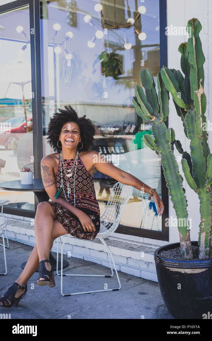 Ridere nero donna seduta al di fuori di un coffee shop Foto Stock