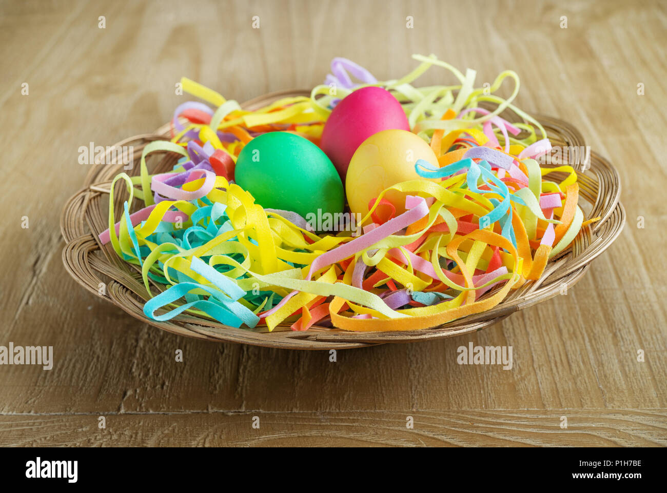 Multi colore uova di pasqua in un cesto su vintage sfondo di legno Foto Stock