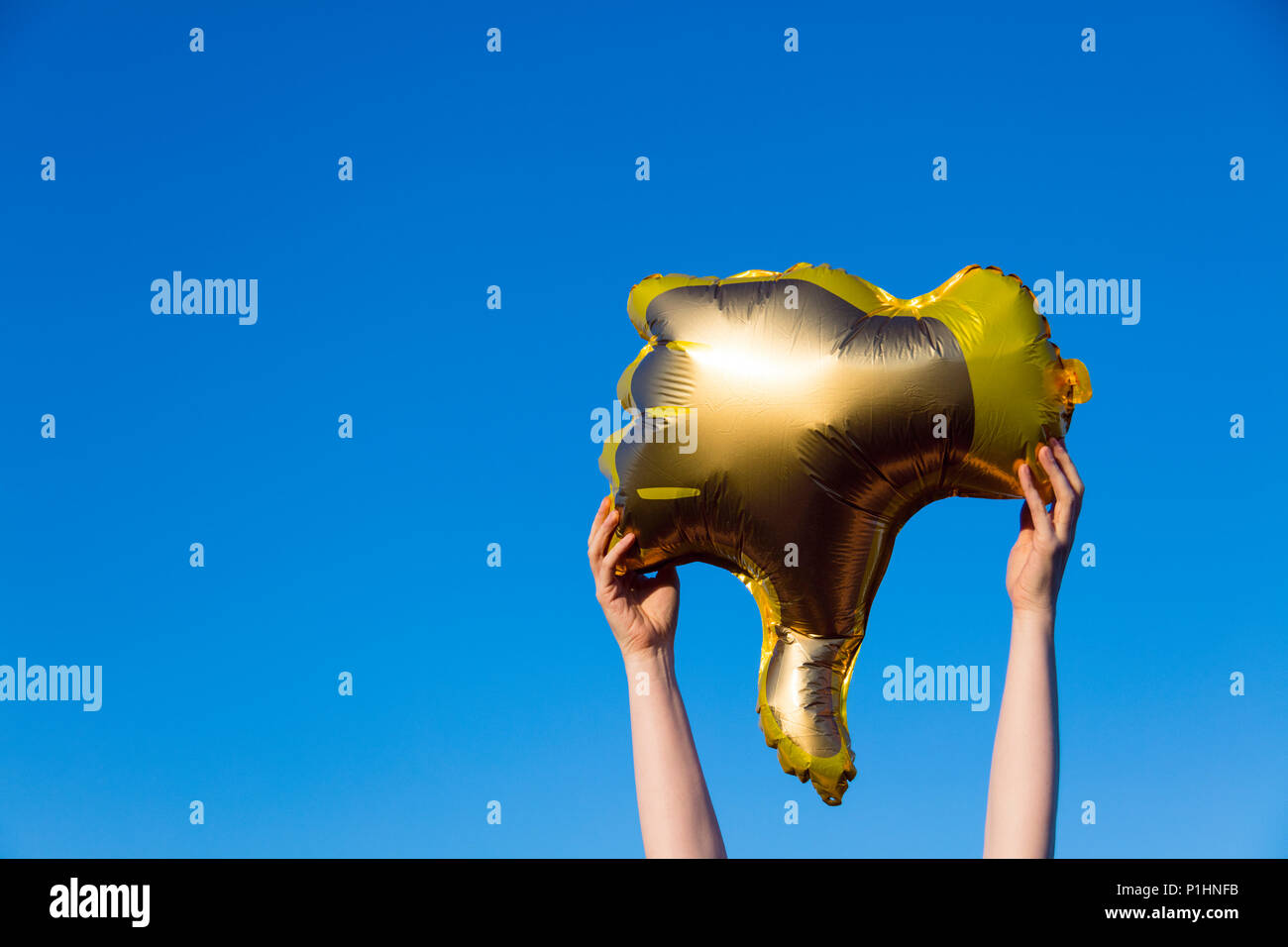 Golden pollici giù antipatia palloncino tenuta contro un luminoso Cielo di estate blu Foto Stock
