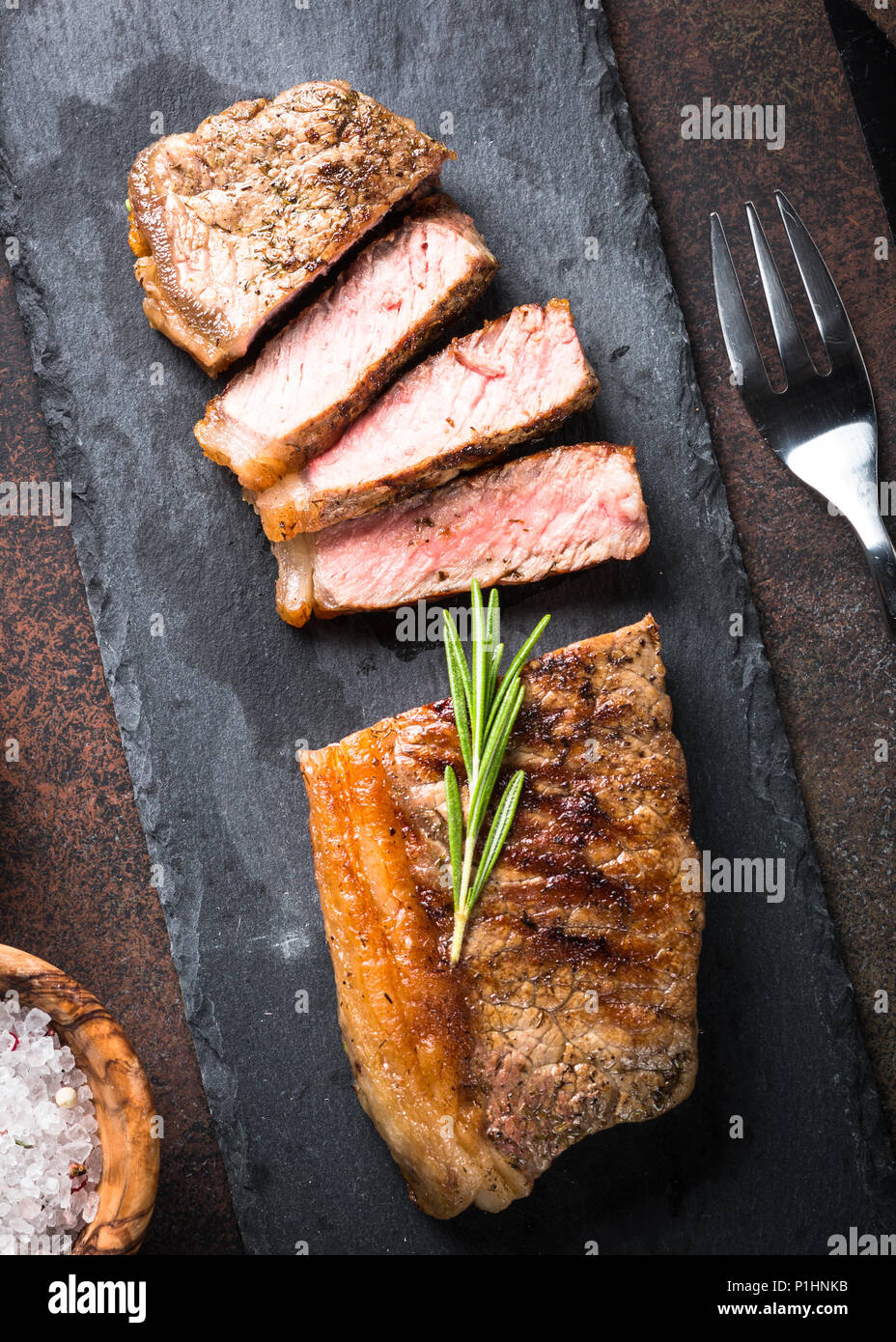 Bistecca di manzo. Alla brace bistecca di controfiletto sul tagliere con rosmarino. Vista dall'alto. Foto Stock