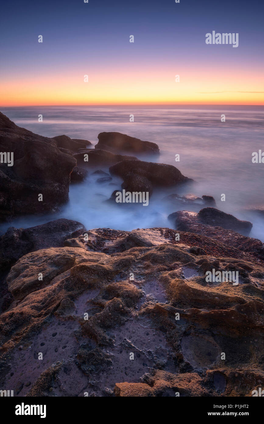 Rocce e onde in tempo di esposizione lungo durante il tramonto all'Oceano Atlantico, Praia Santa Cruz, Portogallo Foto Stock