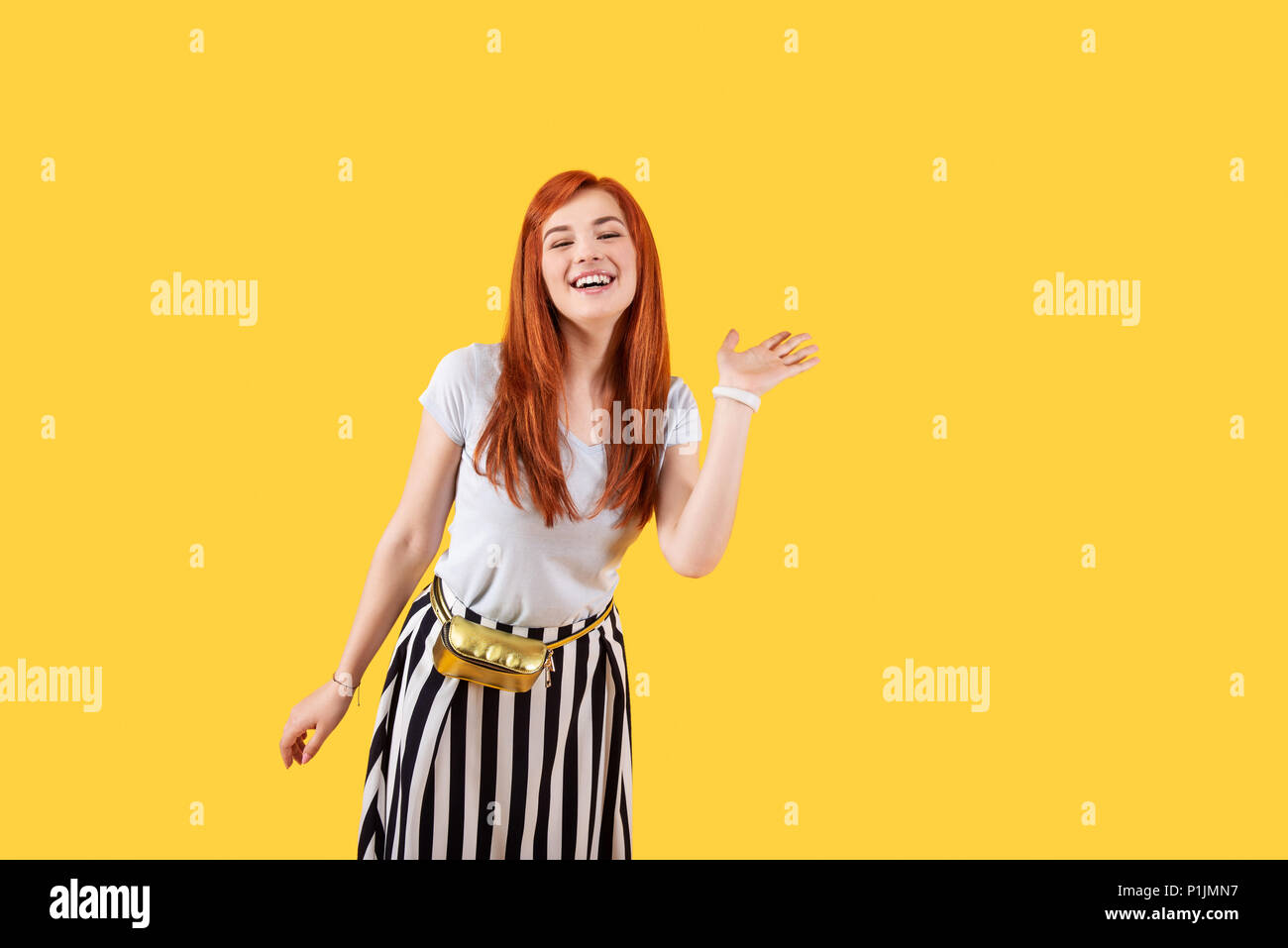 Gioiosa donna attraente in piedi contro sfondo giallo Foto Stock