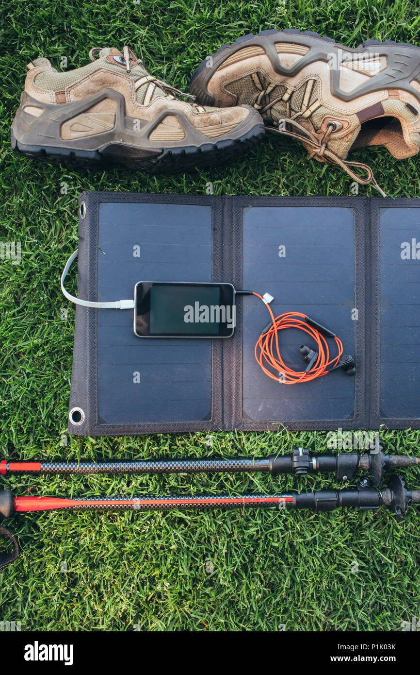 Portatile batteria solare,telefono, cuffie, pali trekking, stivali, sull'erba verde , vista dall'alto. Foto Stock