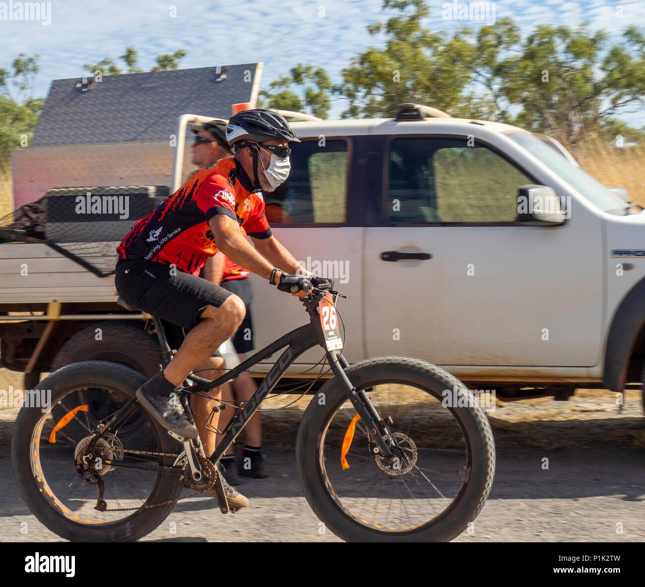 Gibb Challenge 2018 un maschio ciclista in jersey e bib a cavallo di un fatbike passando veicolo di supporto su strada sterrata Gibb River Road WA Kimberley Australia. Foto Stock