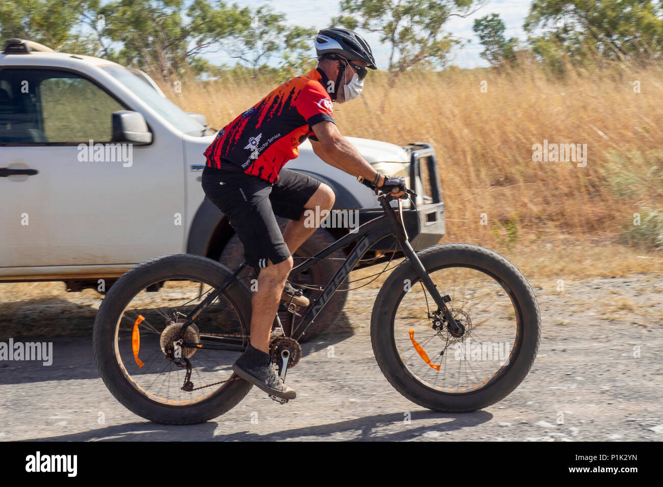 Gibb Challenge 2018 un maschio ciclista in jersey e bib a cavallo di un fatbike passando veicolo di supporto su strada sterrata Gibb River Road WA Kimberley Australia. Foto Stock