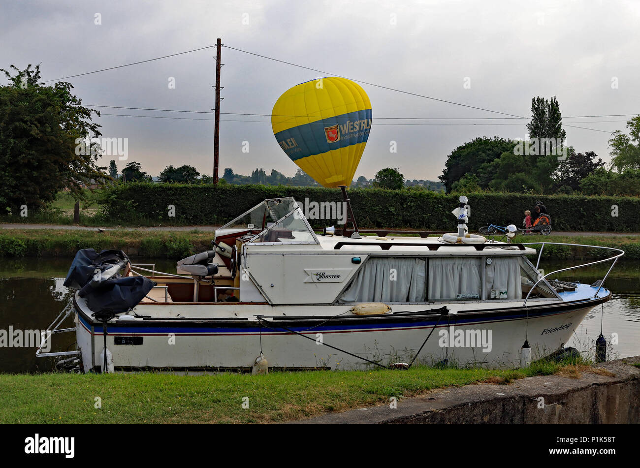 Un grande giallo mongolfiera atterra in un agricoltore il campo sul lato opposto del Leeds e Liverpool canal al di là di un incrociatore ormeggiato in barca Foto Stock