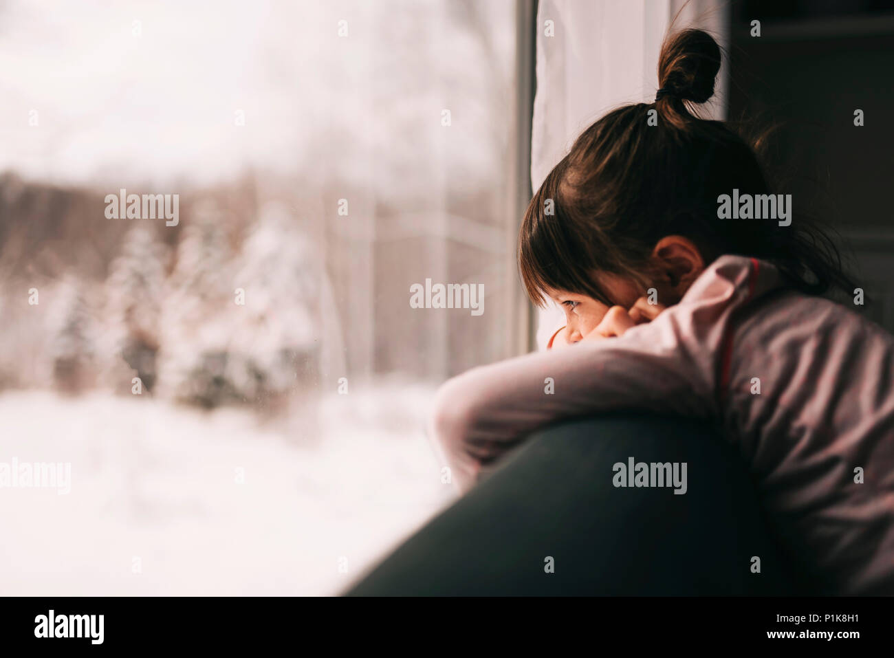 Ragazza appoggiata su un divano guardando fuori della finestra Foto Stock