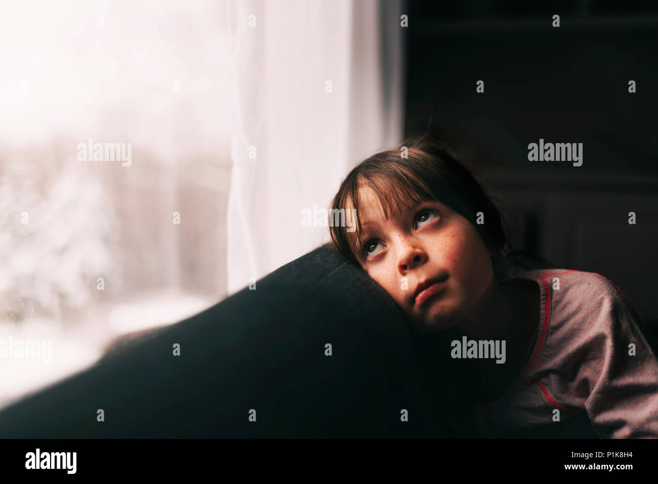 Ragazza seduta su un divano guardando attraverso una finestra Foto Stock