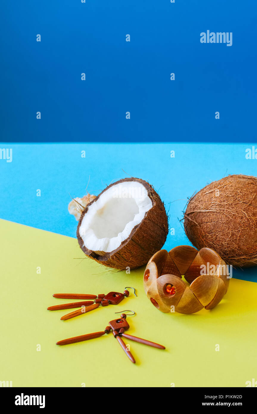 La vacanza estiva, eco e informale in stile concetto. Moda braccialetto di legno e orecchini noci di cocco su sfondo bicromatica. Foto Stock