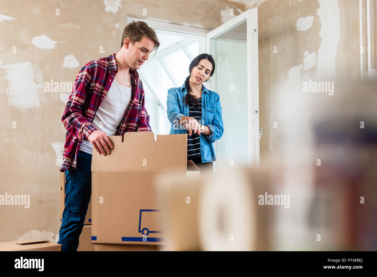 Giovane donna portando un pesante aperto la scatola di cartone mentre si è in movimento con il suo fidanzato nella loro nuova casa Foto Stock