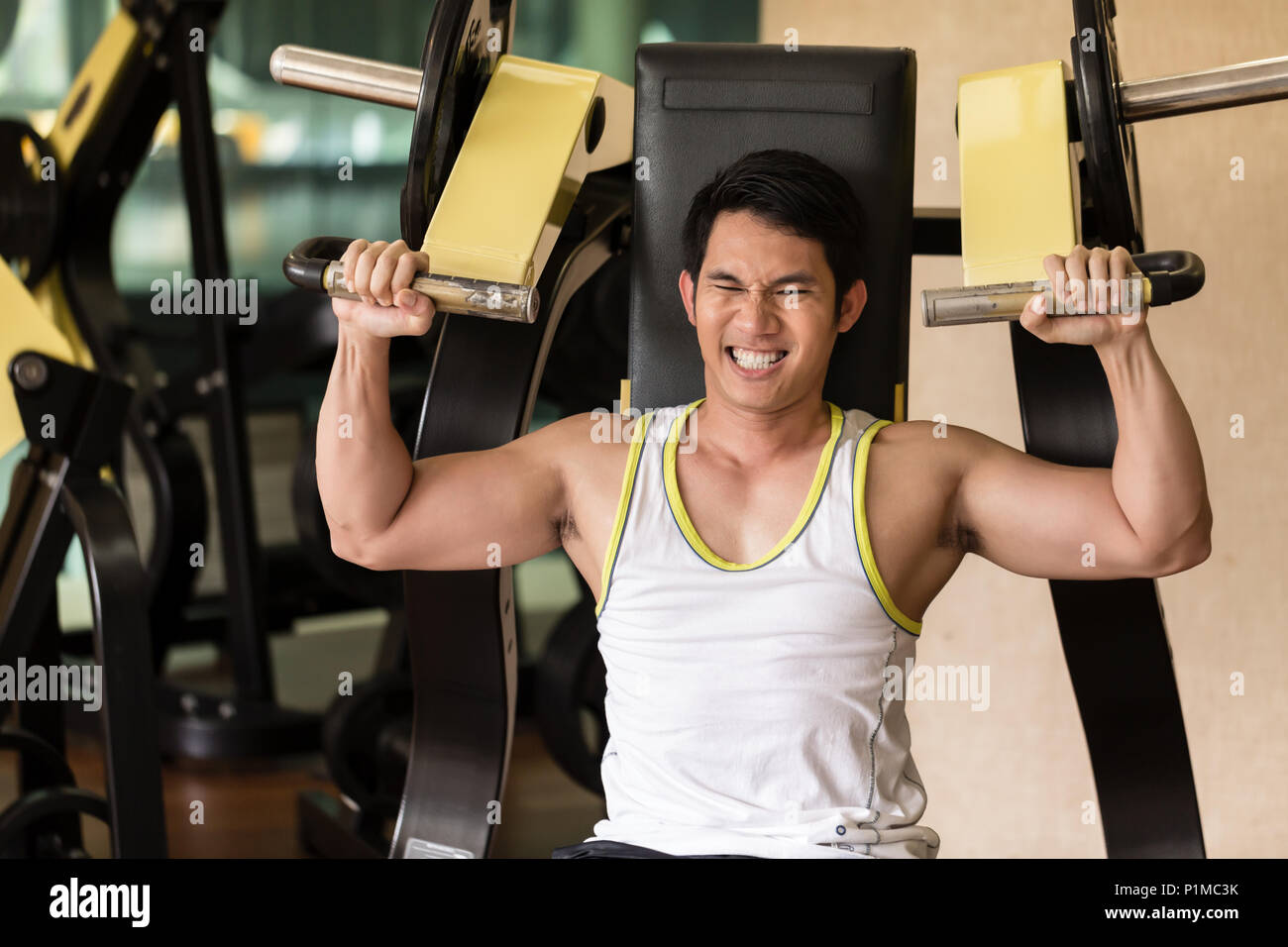 Ritratto di un bello e forte giovane uomo sorridente mentre si esercita per bracci muscoli durante la fase superiore di routine del corpo in corrispondenza di un club fitness con moderne equipmen Foto Stock