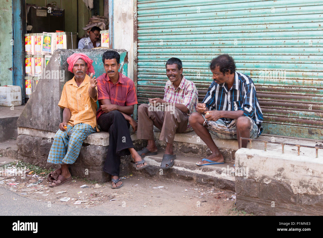 Quattro uomini seduti al di fuori di un negozio con le tapparelle giù a Kochi, Kerala, India. Foto Stock