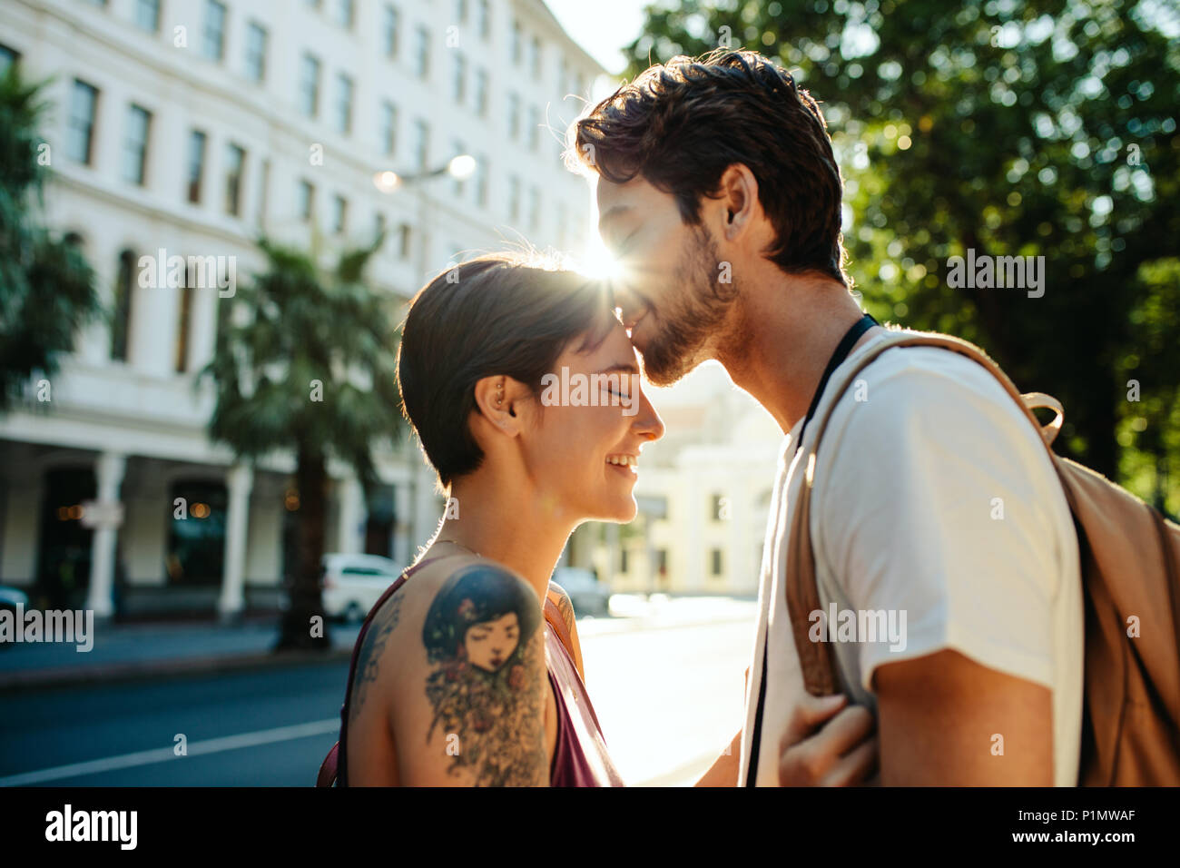 Uomo Donna baciare sulla fronte in piedi sulla strada con Sun in background. Turista giovane in una felice e umore romantico mentre ad esplorare la città. Foto Stock