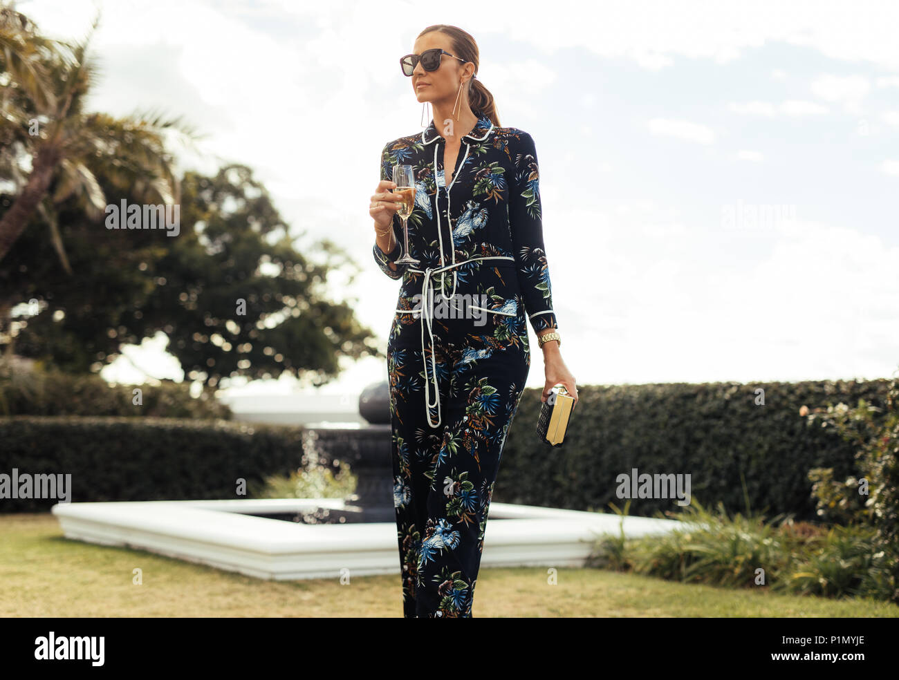 Donna Gorgeous camminando nel prato con un bicchiere di vino. Elegante femmina ricchi con vino escursioni all'aperto. Foto Stock
