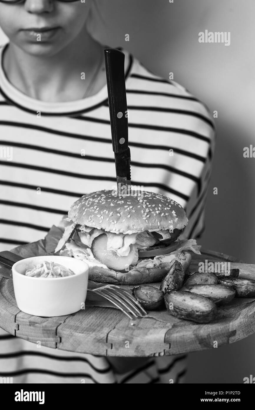 Donna vestita di ponticello a strisce holding round piatto in legno con appetitose gioco servita con pomodorini, rosmarino e salsa giacente sul pezzo di kra Foto Stock