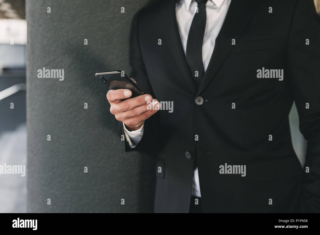Immagine ritagliata di un imprenditore vestito in tuta in piedi al di fuori di un edificio di vetro e tenere il telefono cellulare Foto Stock