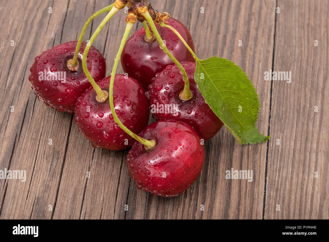 Mazzetto di lavata di ciliege dolci su uno sfondo di legno. Prunus avium. Bella fresca di bacche rosse di close-up. Pietra sani frutti, foglia verde, gocce d'acqua. Foto Stock