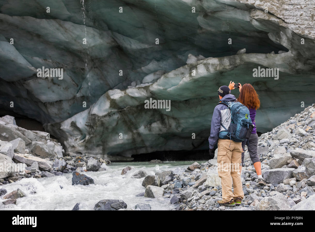 Una donna prende una fotografia di una caverna di ghiaccio con il suo telefono cellulare durante le escursioni al ghiacciaio Gulkana con suo marito; Alaska, Stati Uniti d'America Foto Stock