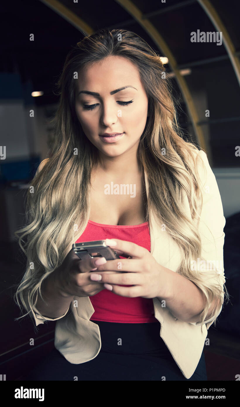 Giovani aziende millenaria donna nel suo posto di lavoro utilizzando un telefono intelligente; Sherwood Park, Alberta, Canada Foto Stock