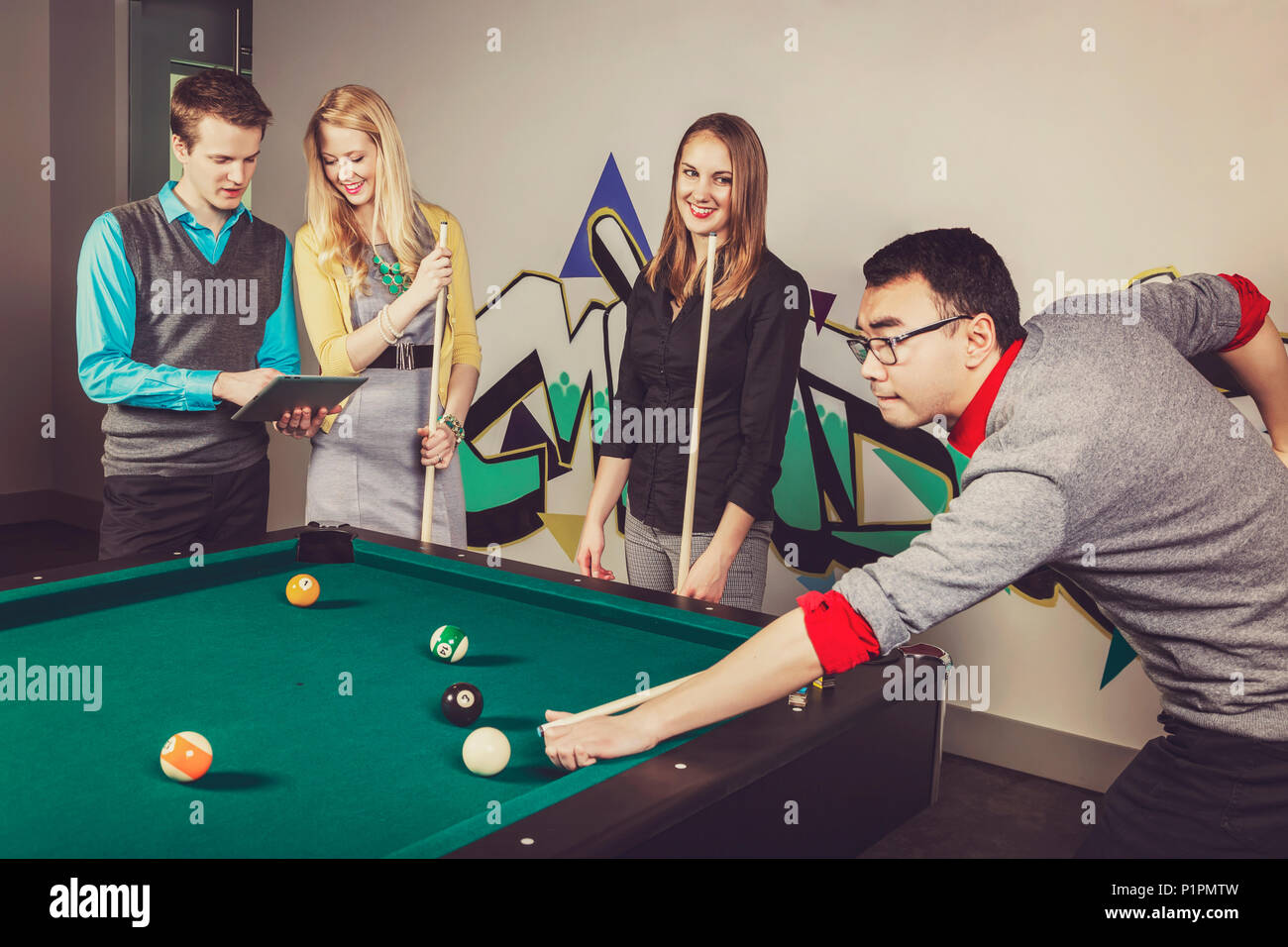 Un gruppo di giovani millenario professionisti aziendali a giocare a biliardo insieme su una pausa di lavoro; Sherwood Park, Alberta, Canada Foto Stock