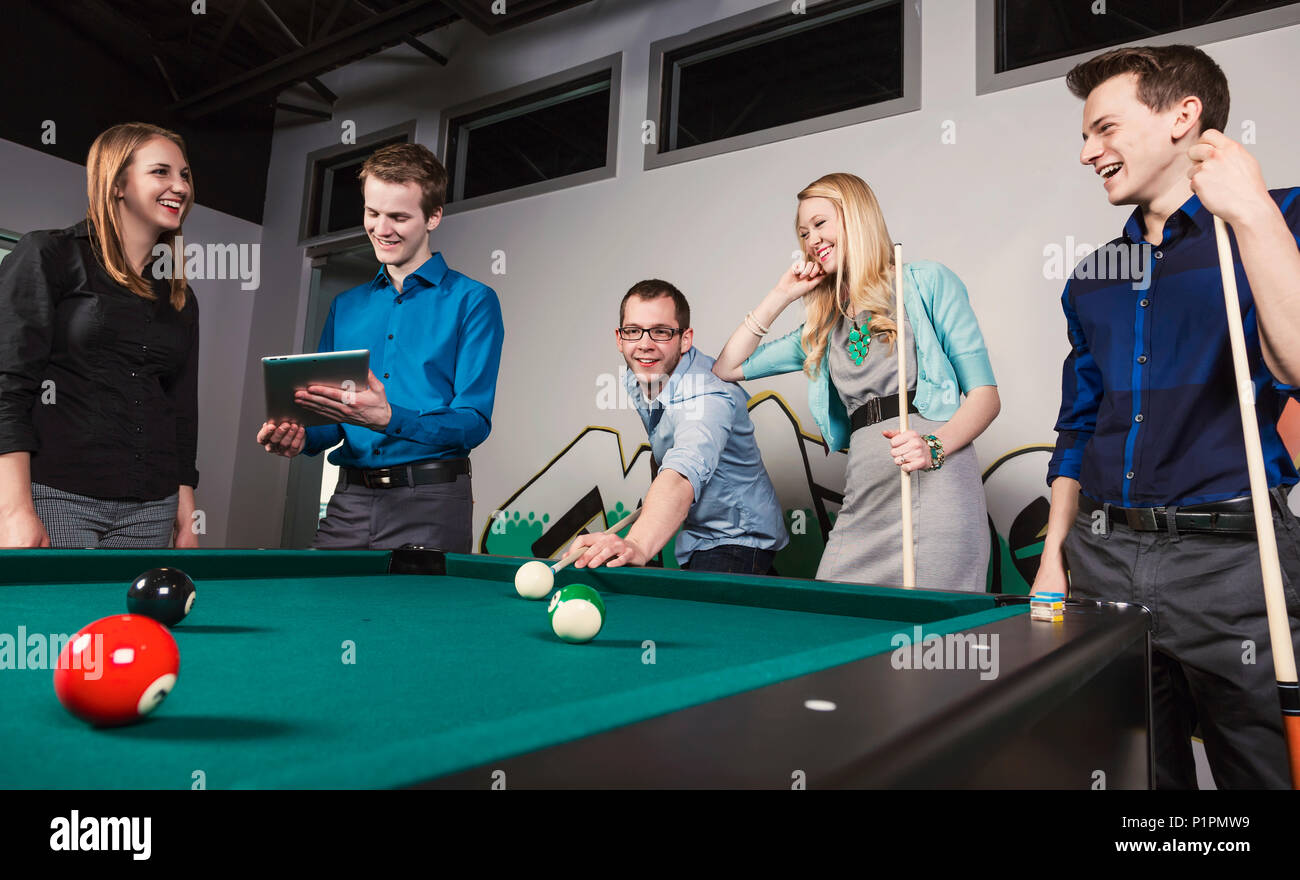 Un gruppo di giovani millenario professionisti aziendali a giocare a biliardo insieme su una pausa di lavoro; Sherwood Park, Alberta, Canada Foto Stock