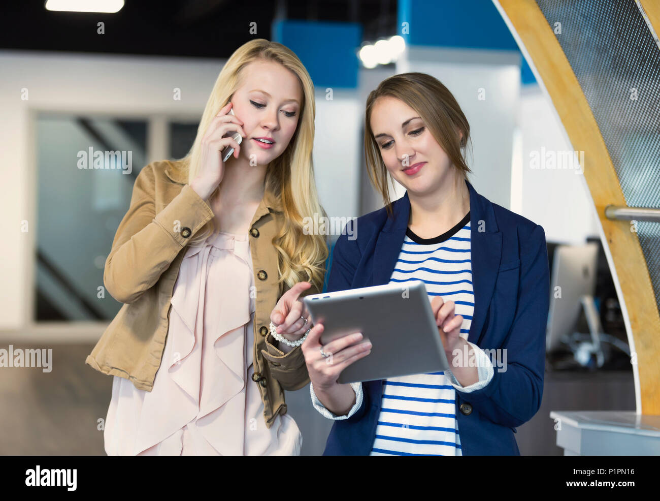 Due belle giovani millenaria delle donne di business utilizzando la tecnologia sul posto di lavoro; Sherwood Park, Alberta, Canada Foto Stock