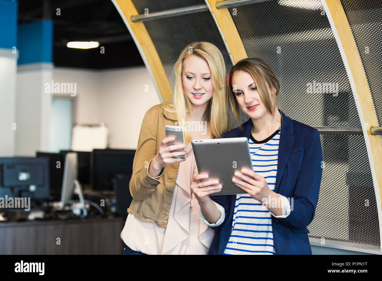 Due belle giovani millenaria delle donne di business utilizzando la tecnologia sul posto di lavoro; Sherwood Park, Alberta, Canada Foto Stock