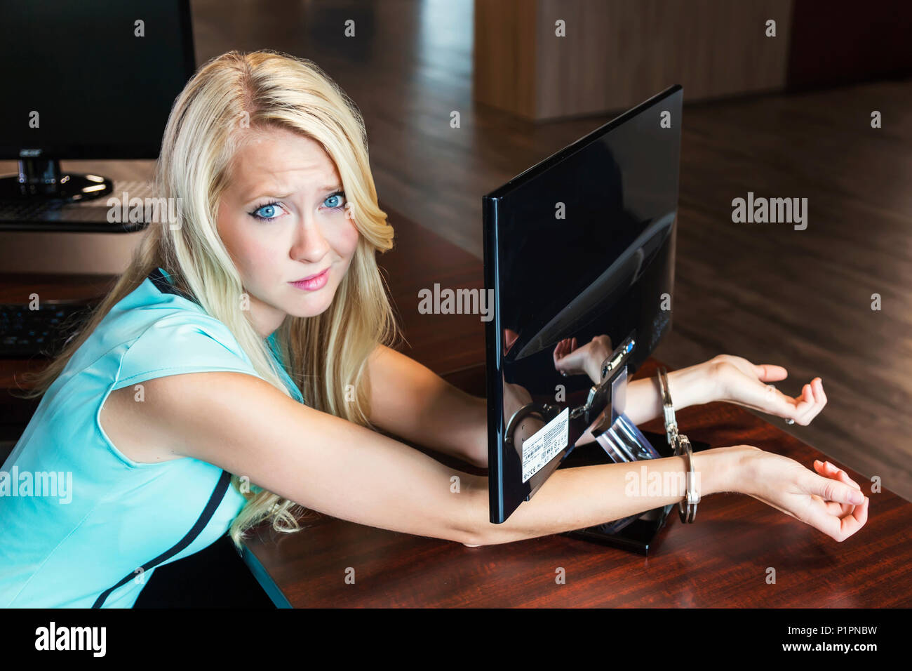 Giovani millenaria business donna ammanettato al suo monitor del computer sul posto di lavoro; Sherwood Park, Alberta, Canada Foto Stock