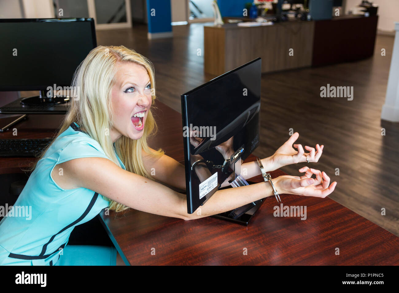 Giovani millenaria business donna ammanettato al suo monitor del computer sul posto di lavoro; Sherwood Park, Alberta, Canada Foto Stock