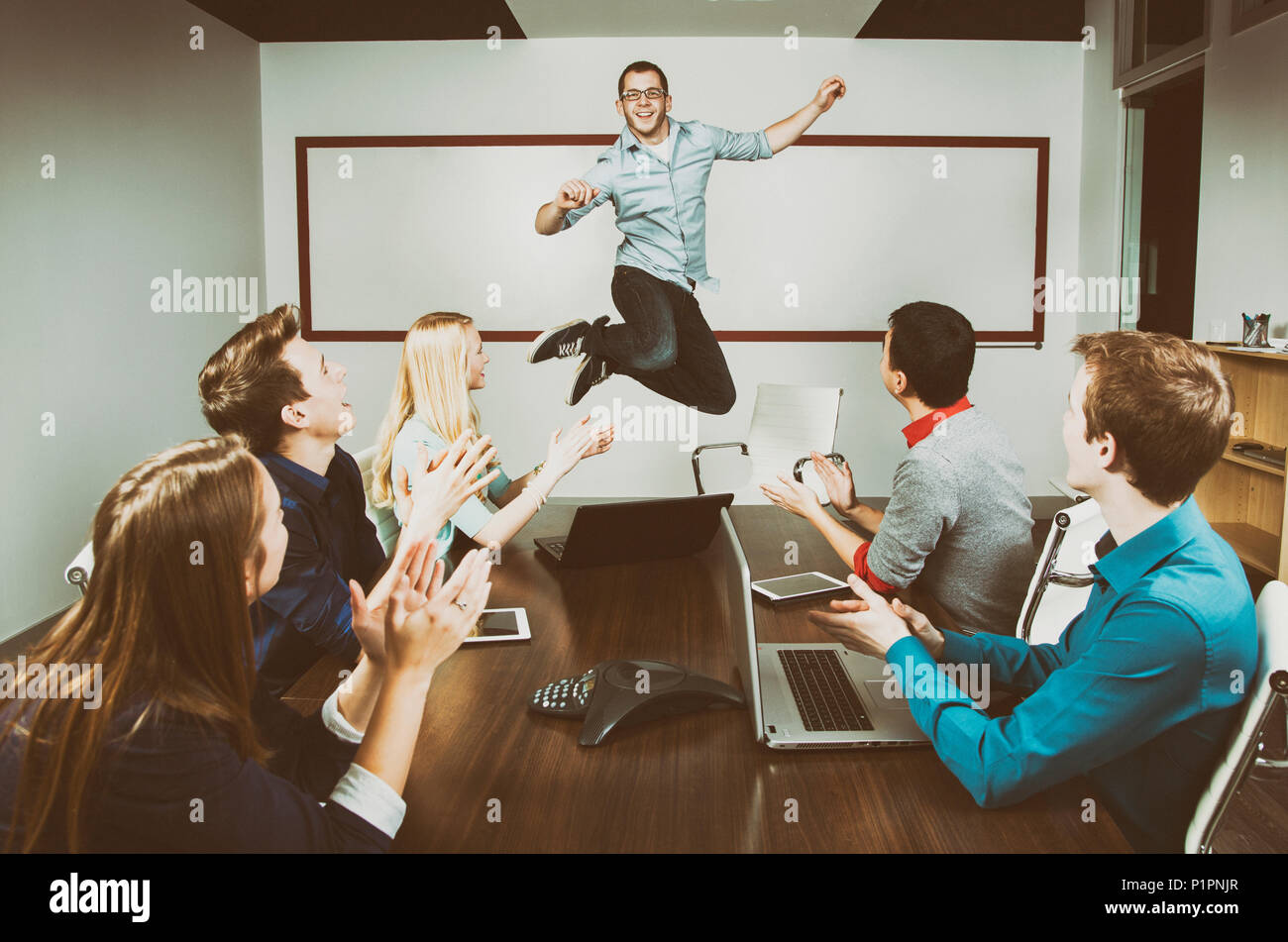 Giovane professionista di affari millennial che salta per celebrare un successo con i suoi collaboratori che lavorano in una sala conferenze durante un presentatio... Foto Stock