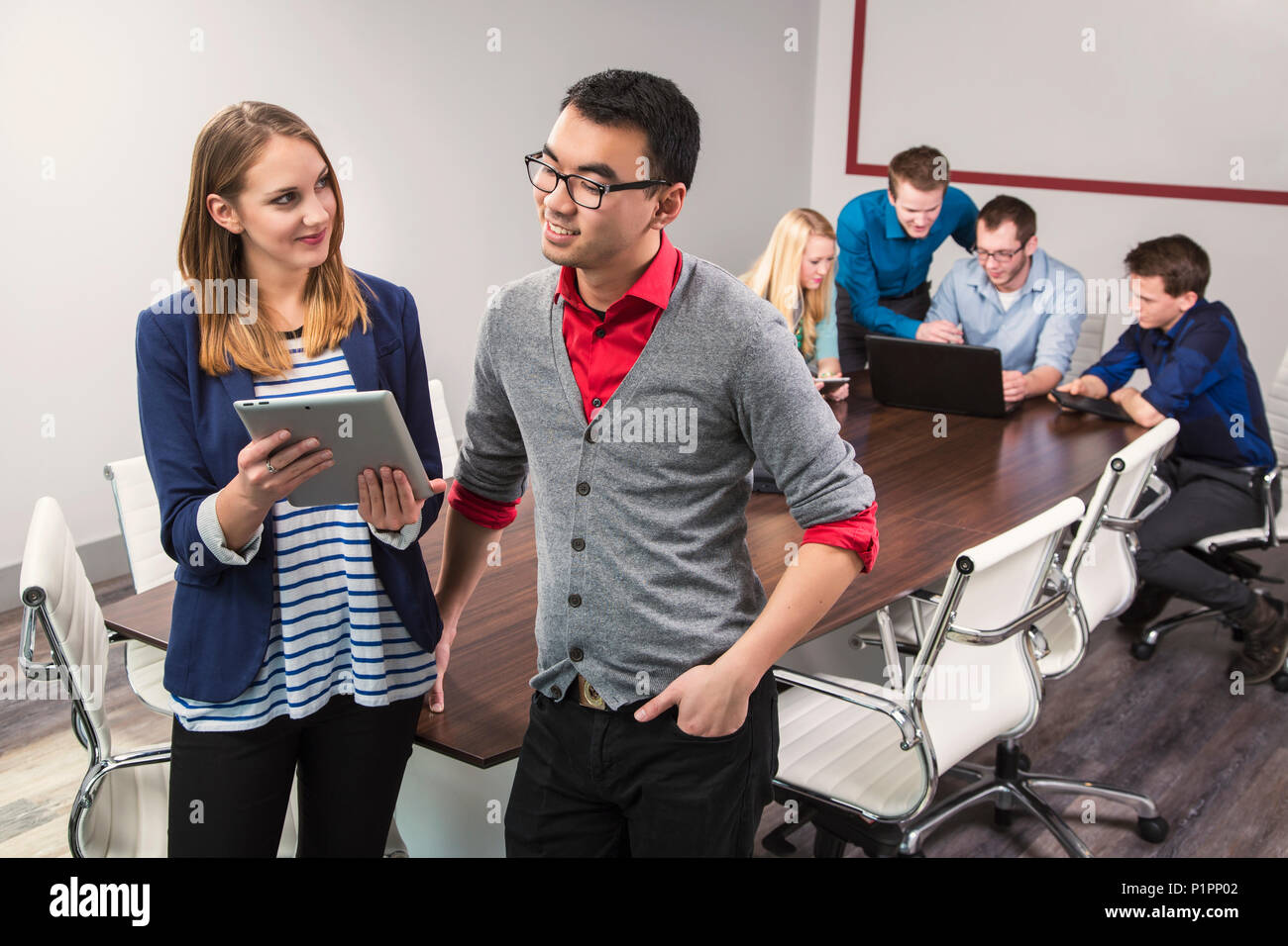 Due giovani millenario professionisti aziendali guardando un tablet mentre si lavora insieme in una sala conferenze con i loro coetanei Foto Stock