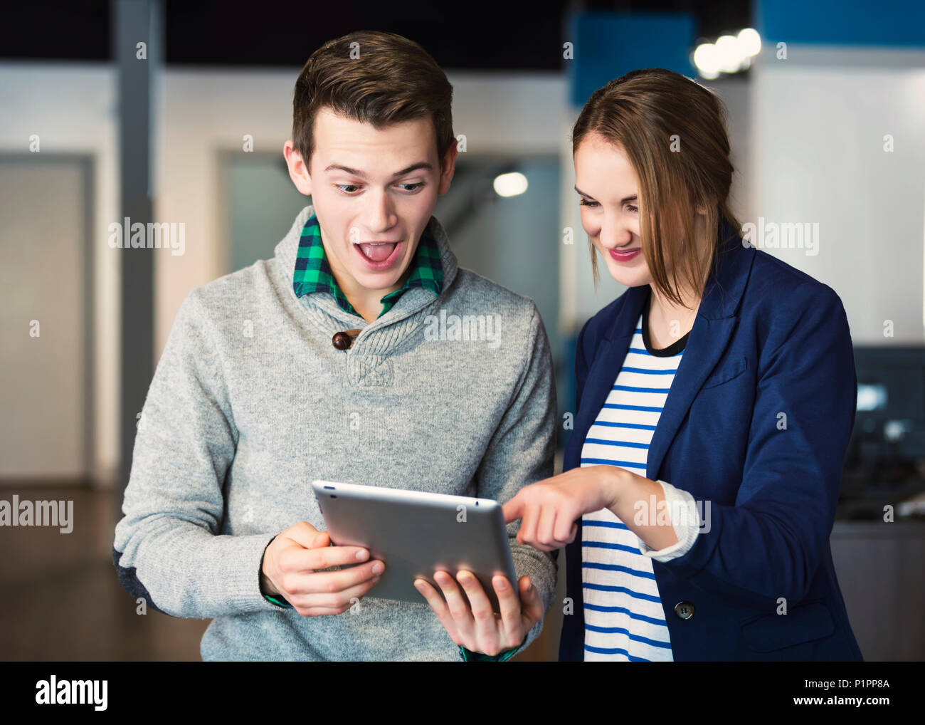 Due giovani millenario professionisti aziendali surpirsed da ciò che vedono sul tablet sul loro posto di lavoro; Sherwook Park, Alberta, Canada Foto Stock