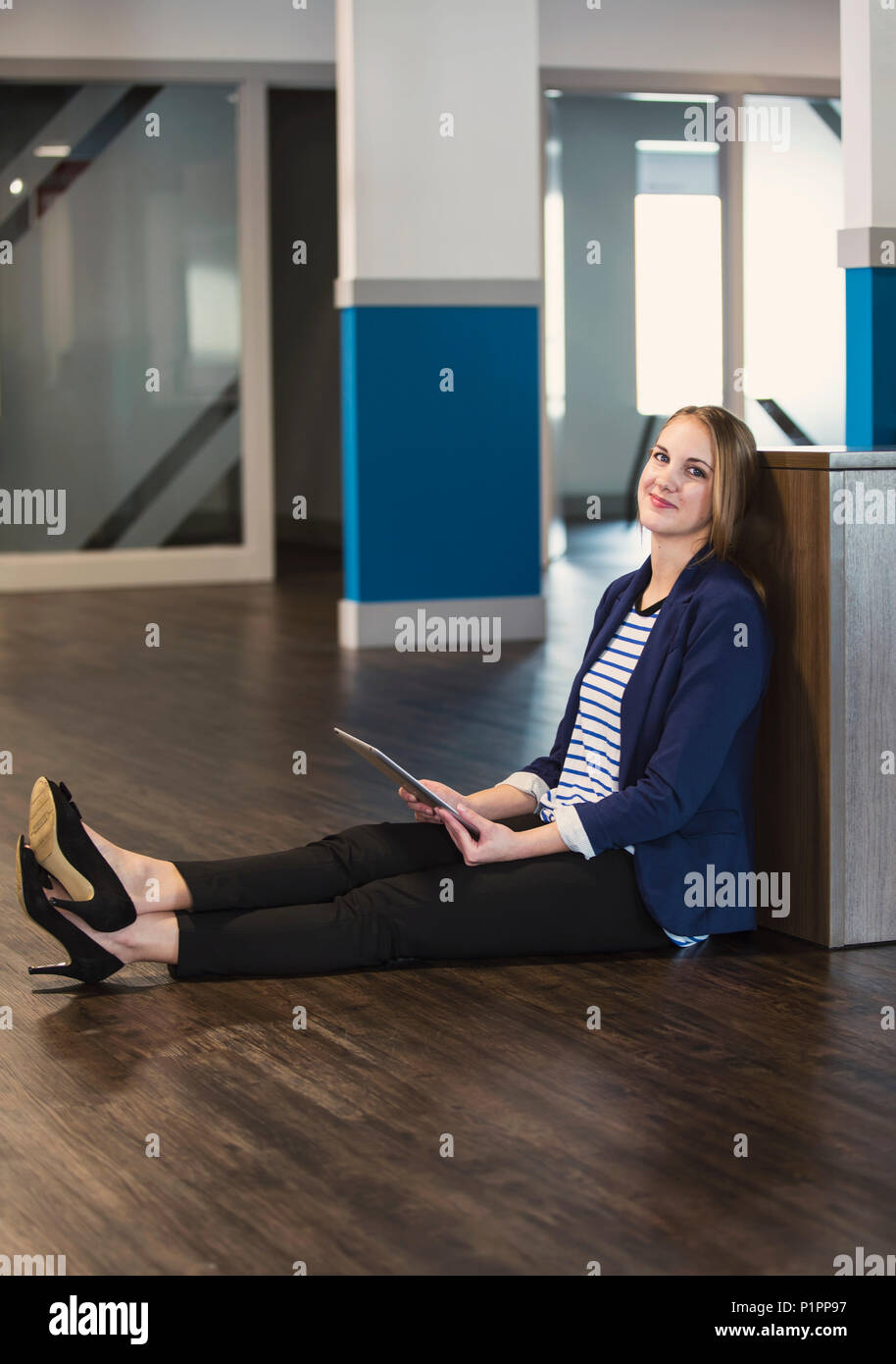 Ritratto di un giovane professionista millenario imprenditrice utilizzando la tecnologia sul posto di lavoro mentre è seduto sul pavimento; Sherwood Park, Alberta, Canada Foto Stock