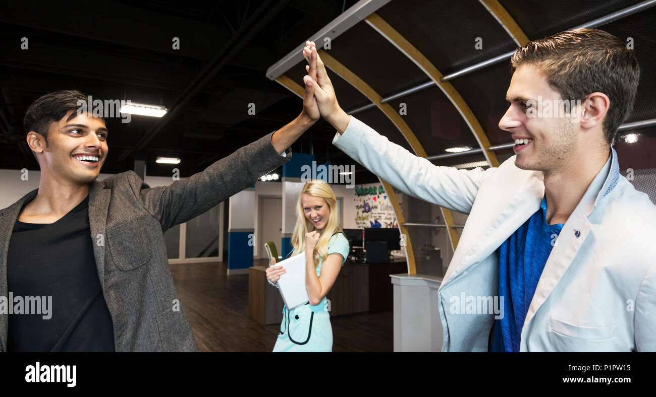 Giovani aziende millenario co-lavoratori di celebrare un successo con una alta cinque sul posto di lavoro; Sherwood Park, Alberta, Canada Foto Stock