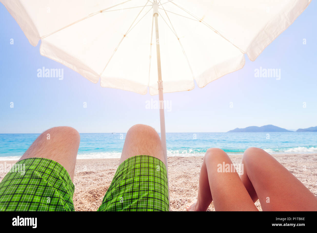 Ombrellone sulla spiaggia e le gambe dei due popoli Foto Stock