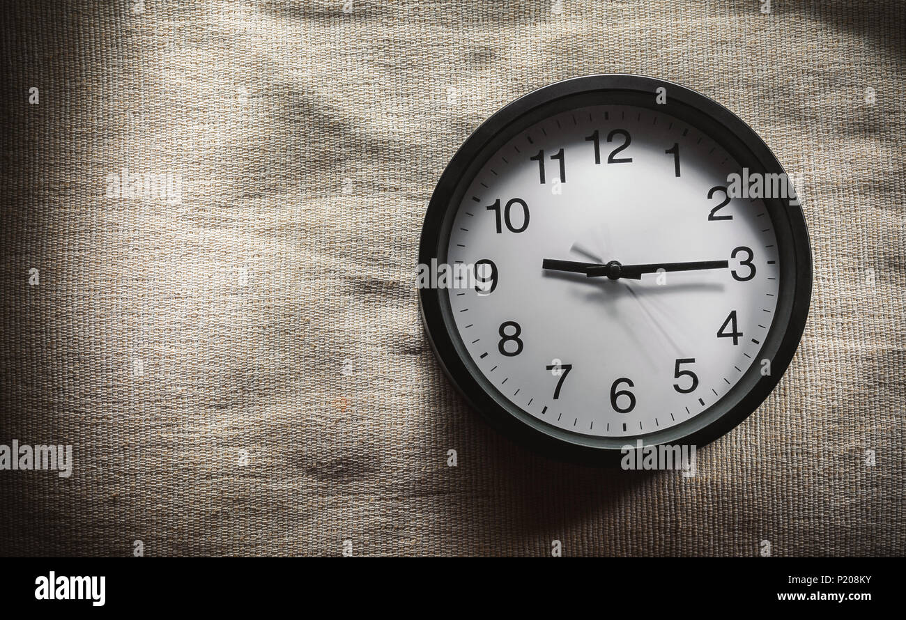 Una composizione semplice, orologio da parete nero sulla coperta del letto che mostra trimestre passato nove ore. Foto Stock