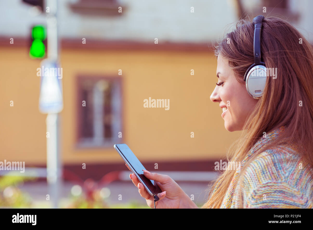 Donna con cuffie per ascoltare musica sul telefono cellulare a piedi  attraversando via sulla luce verde Foto stock - Alamy
