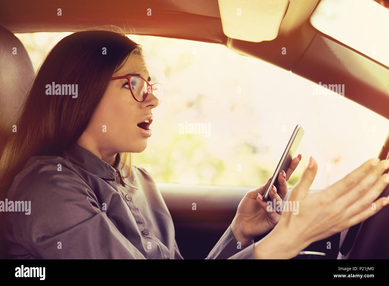 Scioccato donna distratto dal telefono cellulare SMS mentre è alla guida di un veicolo Foto Stock
