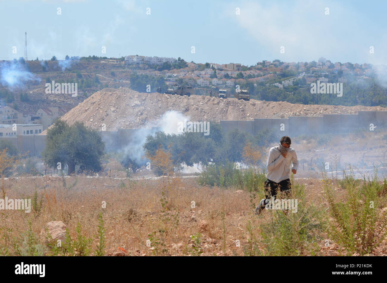 Un manifestante corre da gas lacrimogeni durante le proteste del venerdì. Bilin è un villaggio in Palestina che regolarmente proteste la costruzione dei vicini insediamenti israeliani. La locale popolazione palestinese ritengono insediamenti israeliani sono illegali e che occupano la terra originariamente di proprietà di famiglie palestinesi che vivono nel villaggio. Foto Stock
