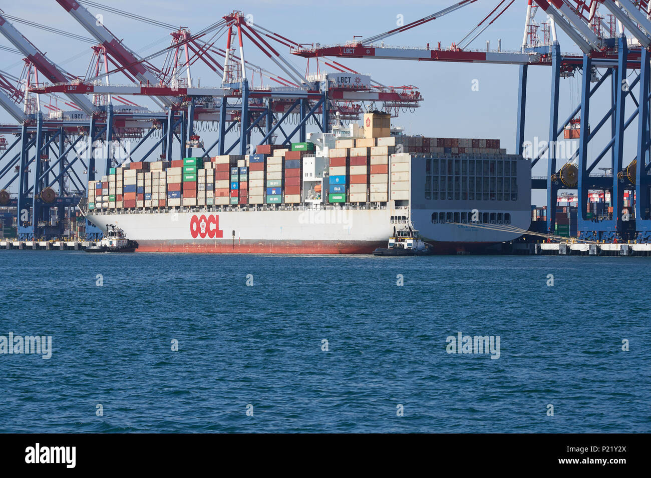 Nave Container, OOCL LONDON, in partenza la lunga spiaggia di terminal per container. Rimorchiatori in attesa di prua e di poppa. Dal porto di Long Beach, California, Stati Uniti d'America. Foto Stock