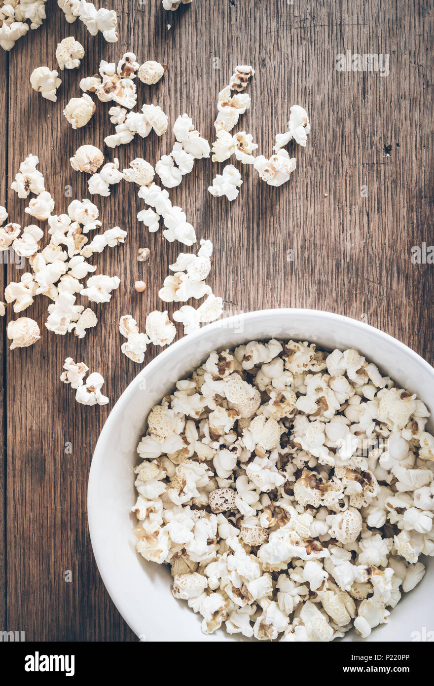 Direttamente sopra il colpo di ciotola riempita con popcorn e popcorn versato su tavola in legno rustico Foto Stock