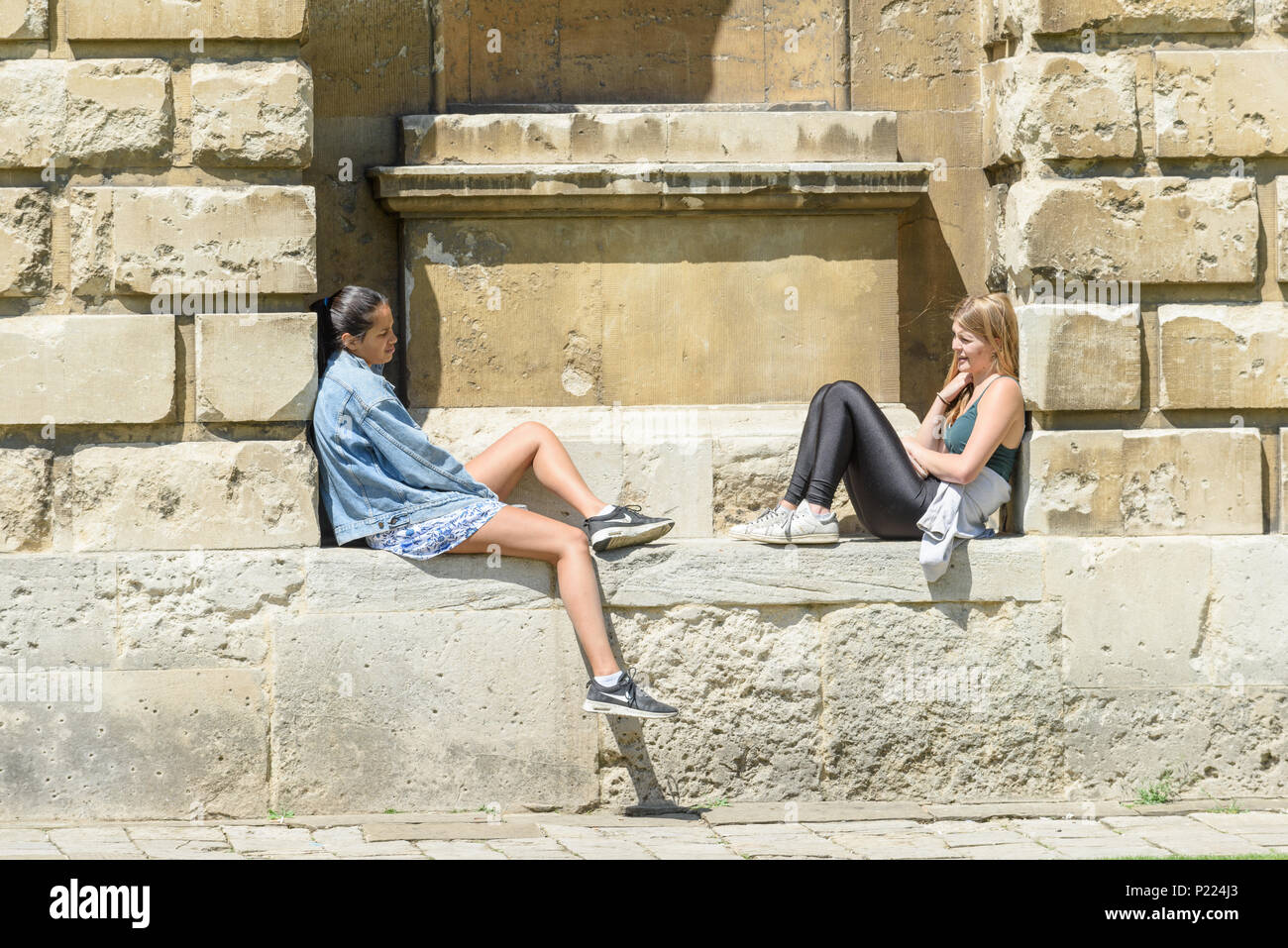 Due studentesse sedersi a parlare su una mensola a Radcliffe Camera biblioteca Bodleian Library durante una soleggiata giornata estiva all'università di Oxford, Inghilterra. Foto Stock