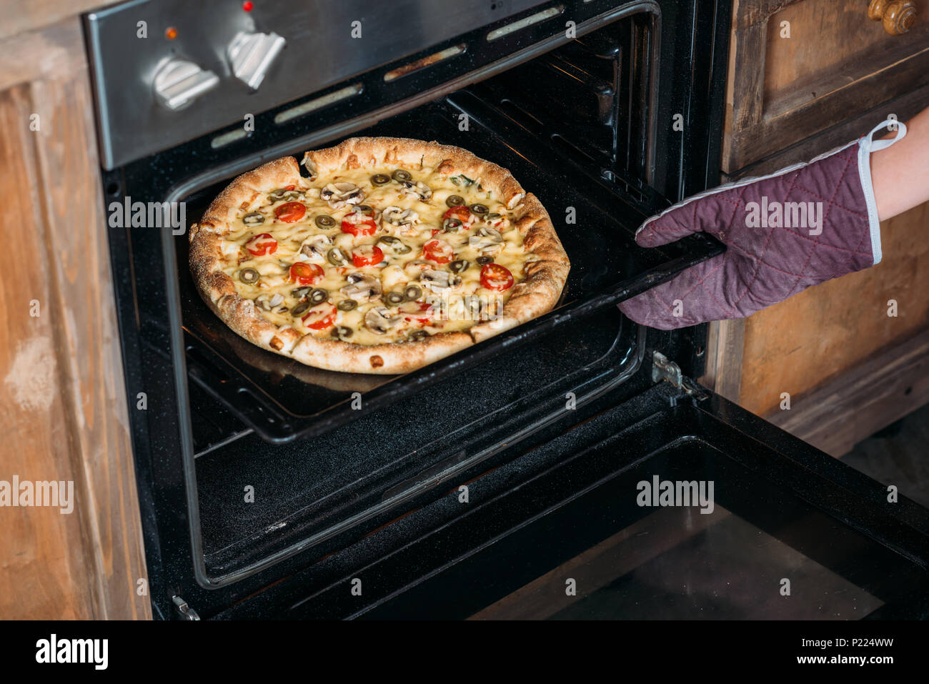 Ritagliato colpo di giovane donna in guanto da forno tenendo la pizza dal forno Foto Stock