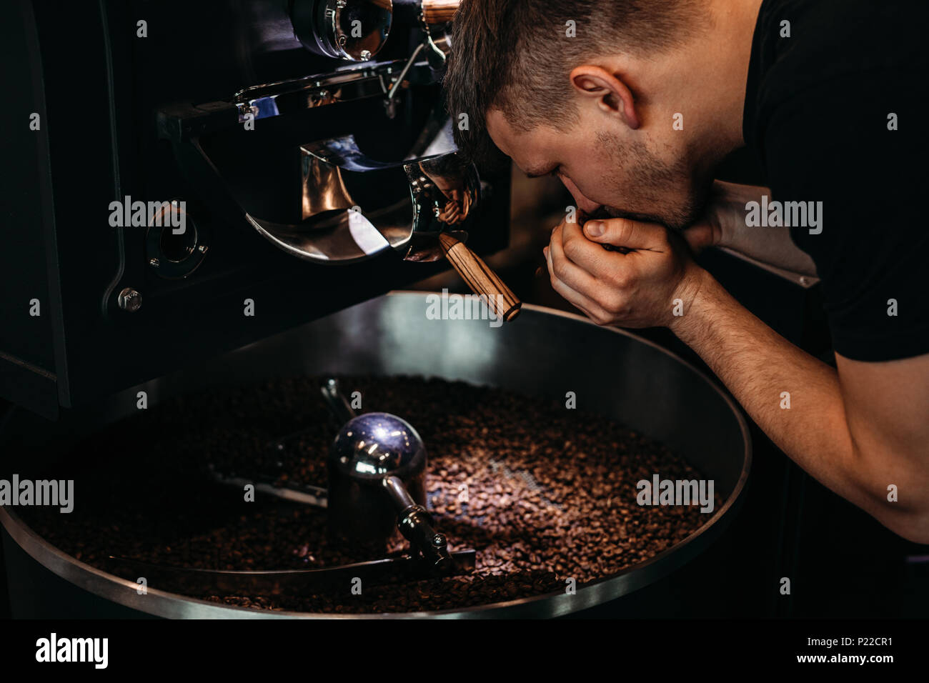 L'Uomo odore di chicchi di caffè, in piedi alla macchina di torrefazione Foto Stock