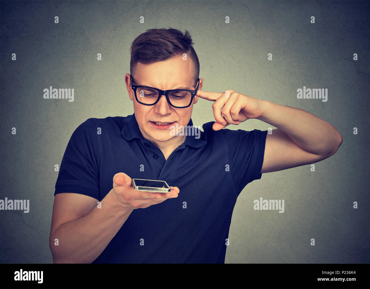 Frustrato uomo utilizzando un telefono intelligente funzione riconoscimento vocale sulla linea isolata sul muro grigio sfondo Foto Stock