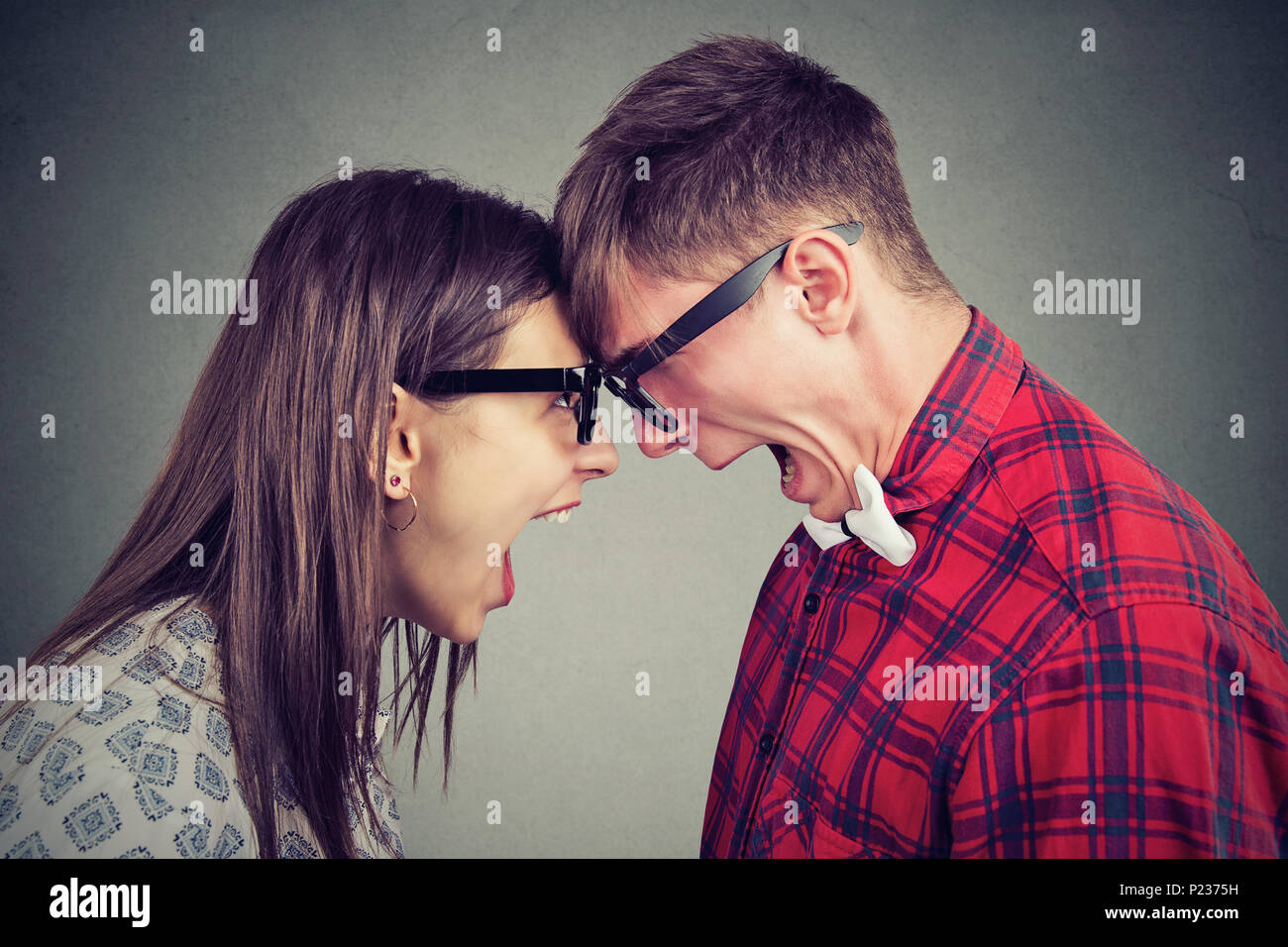 Vista laterale di un uomo e di una donna in bicchieri a urlare contro ogni altra in piedi testa a testa nella diatriba. Foto Stock