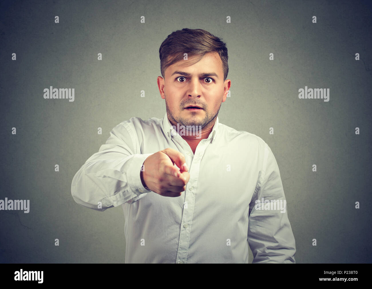Uomo pieno di paura guardando stupiti e puntando alla fotocamera su sfondo grigio. Foto Stock