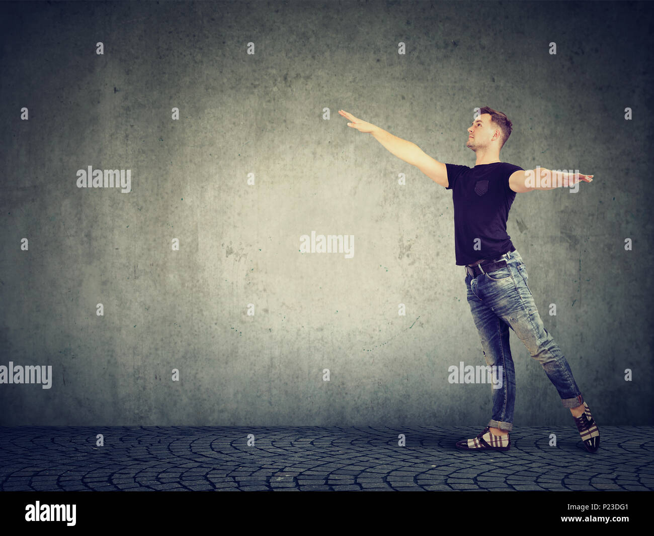 Casual giovane uomo in piedi nel passo di ballo tenendo le mani distanziate e in posa dreamily su grigio. Foto Stock