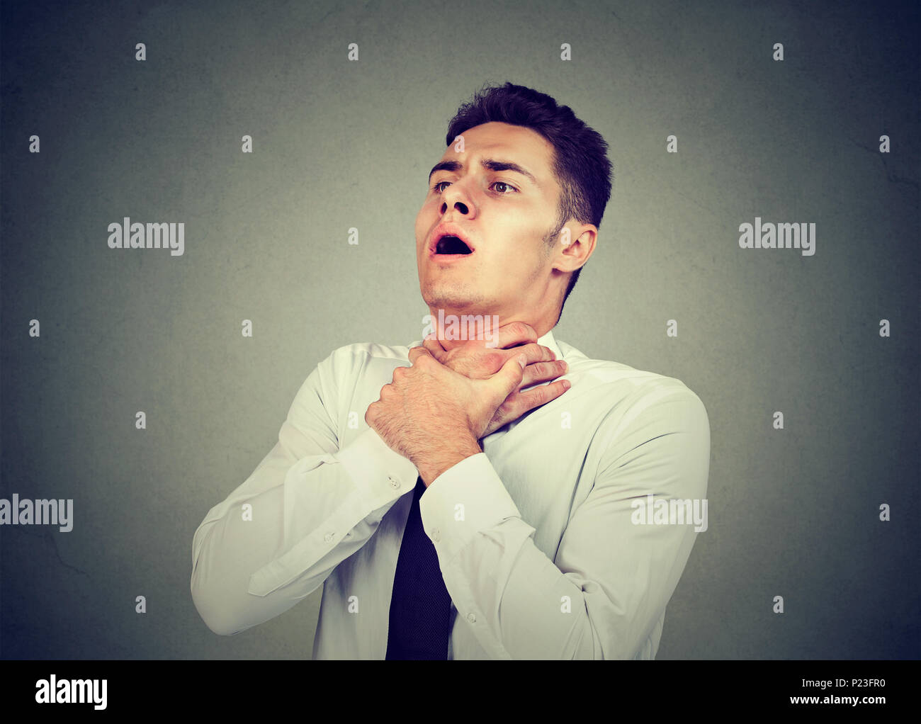 Giovane uomo avente attacchi di asma o parzializzando non respiro che soffre di problemi respiratori isolati su sfondo grigio Foto Stock